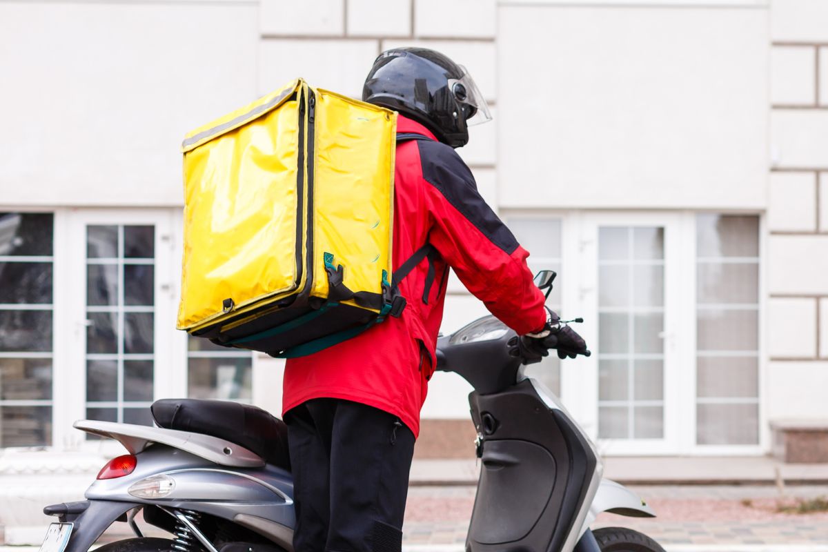 The photo of a delivery man riding with his motorcycle.