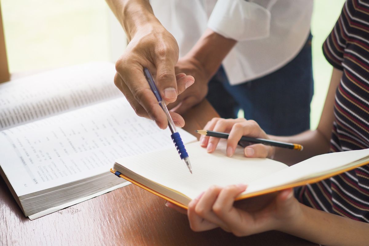 The photo shows a book and a teacher teaching his students.