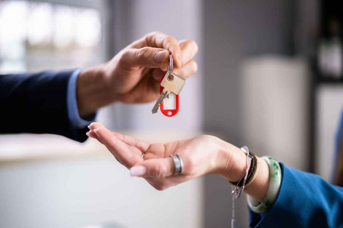 The photo shows a man's hand handing the key to a lady's hand.