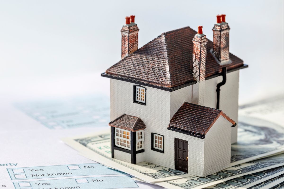 The image of papers, dollar bills, and a mini house for real estate deals.