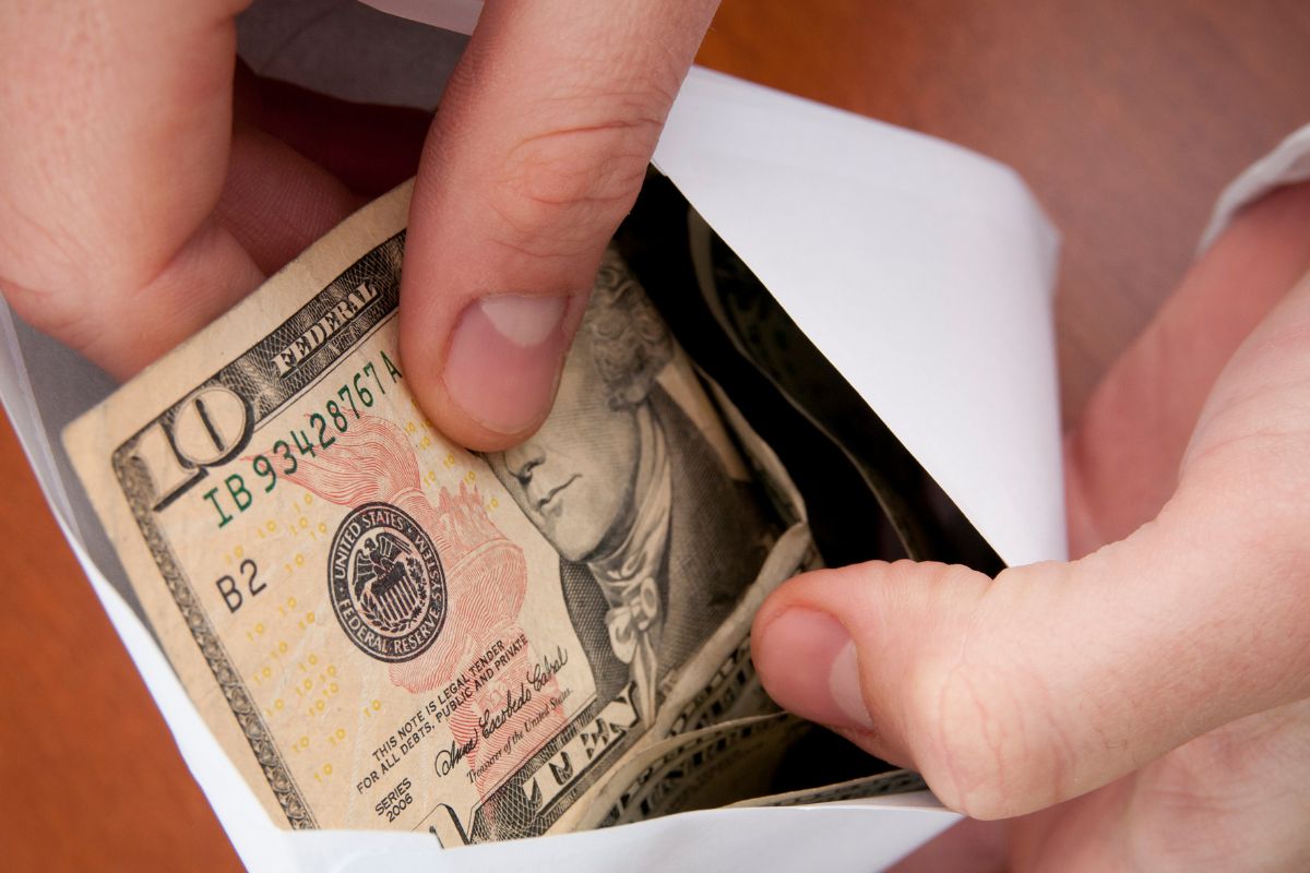 The picture shows a girl's hand holding an envelope with dollar bills.