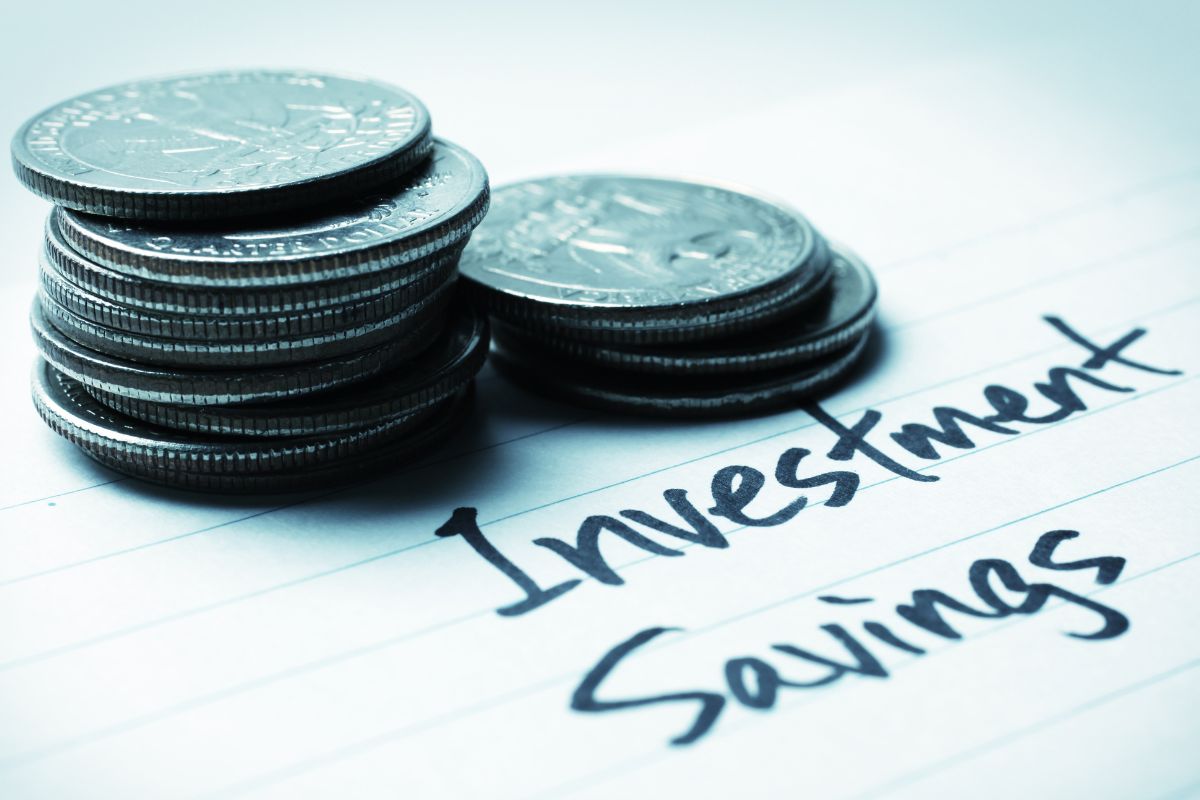 The image shows a stack of coins and a paper with investment and savings wording.