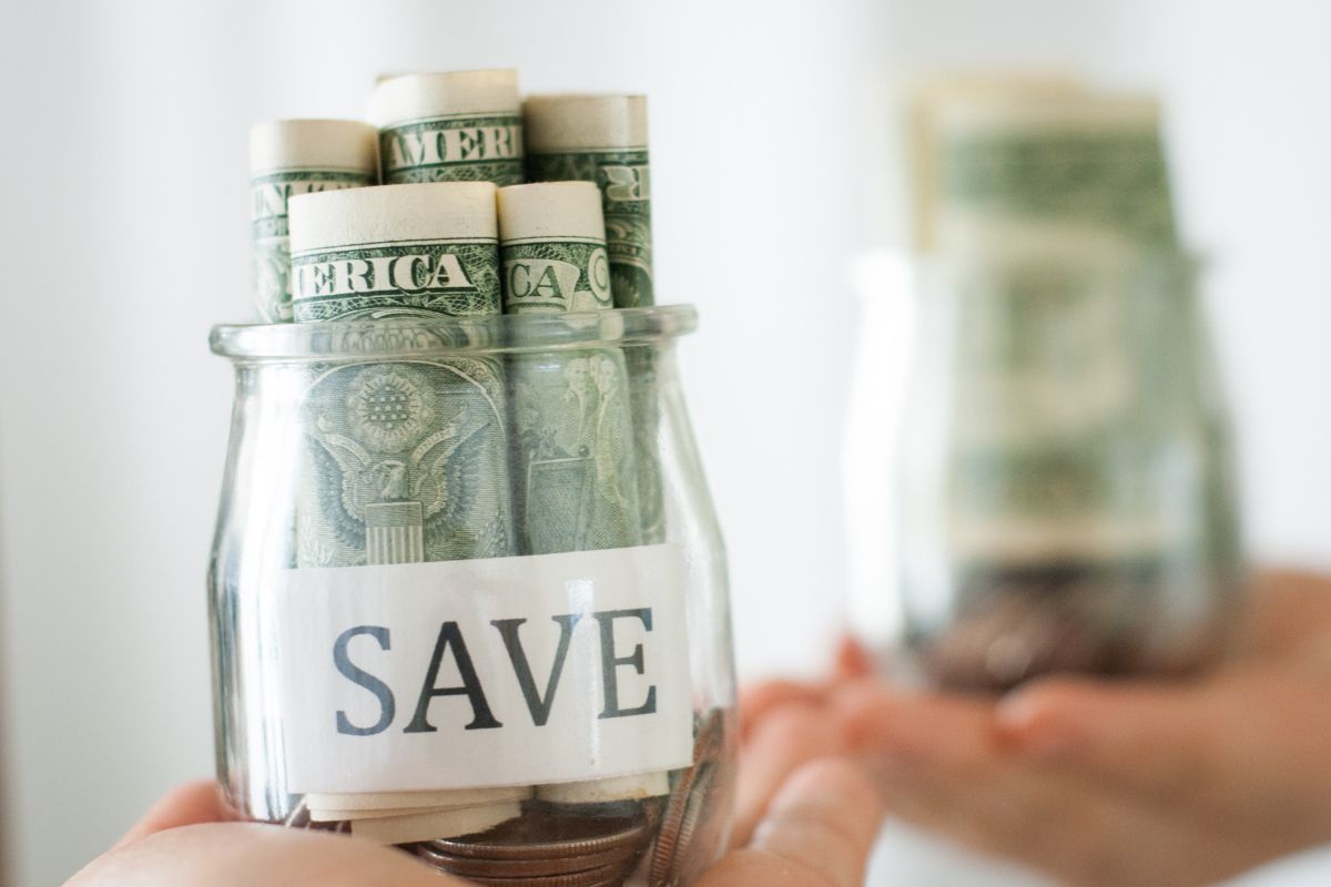 The image of a lady's hand holding a jar filled with dollar bills to pay yourself first.