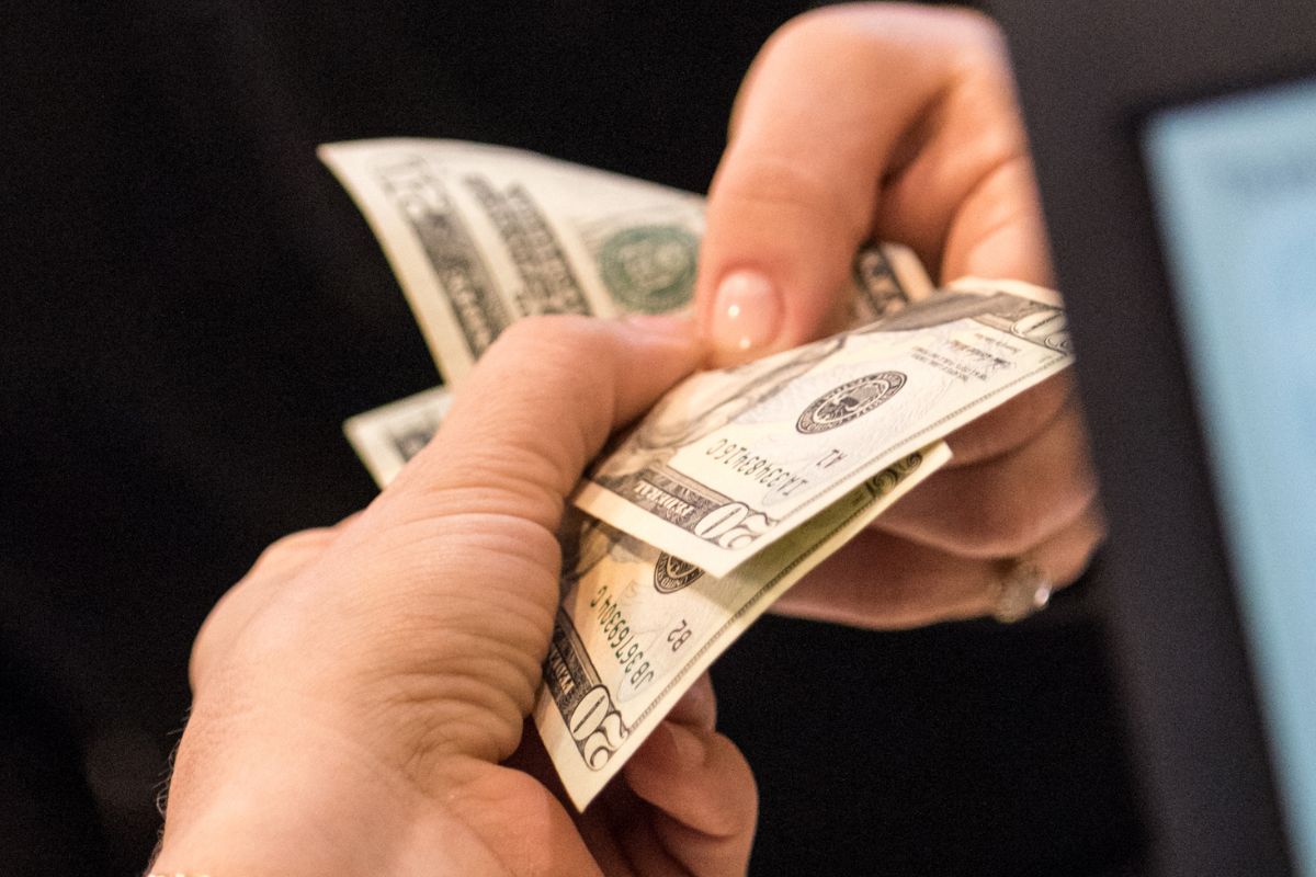 The image shows a customer's hand using cash for nonessential spending.