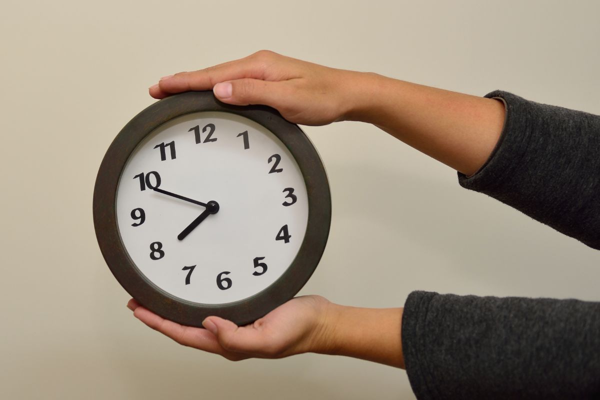 The image shows a young lady's hand holding a clock means delay gratification.