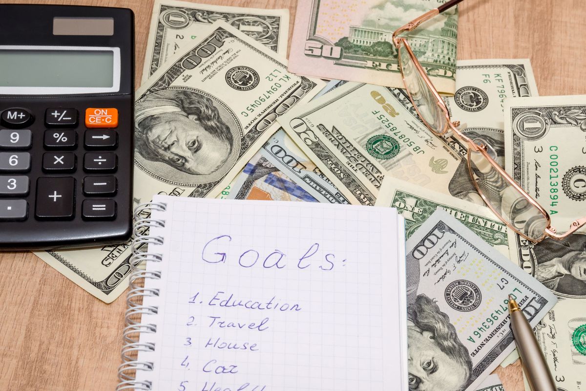 The picture shows dollar bills, a calculator, and a notebook with financial goal lists.