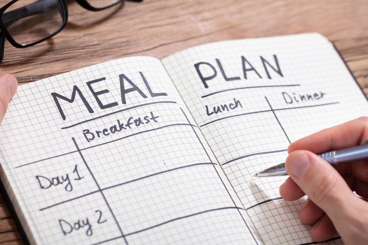 The photo shows a man's hand making a meal plan.