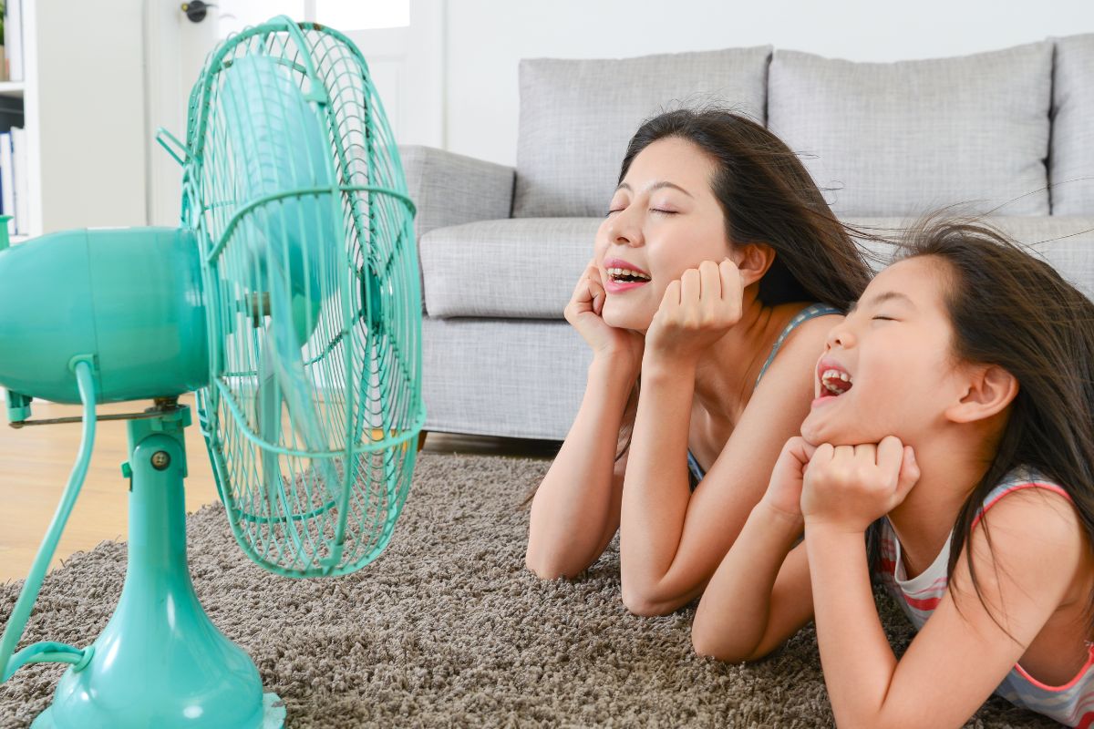 A picture of a mom and a daughter in front of an electric fan. 