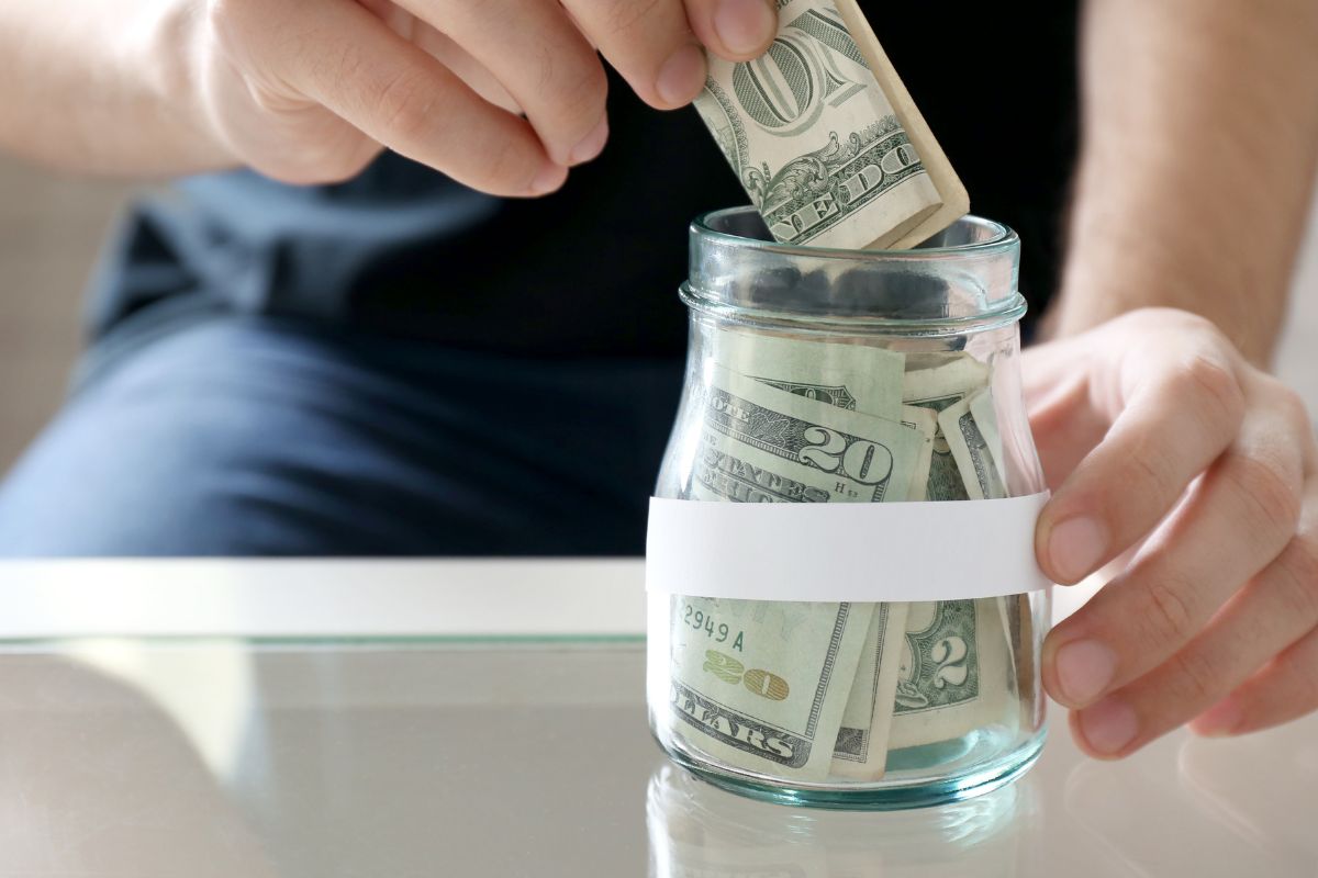 A picture of someone putting one dollar in a jar.