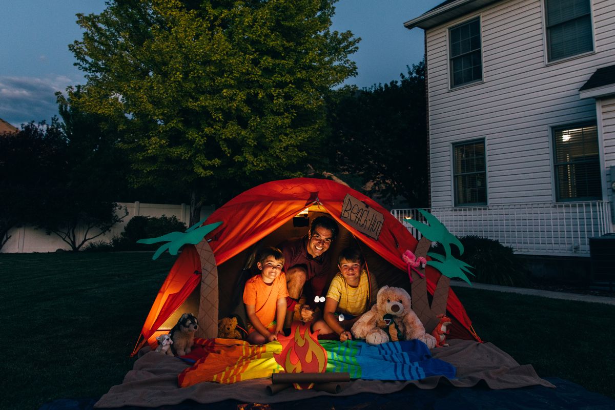 A picture of a father and his kids doing a backyard camping. 