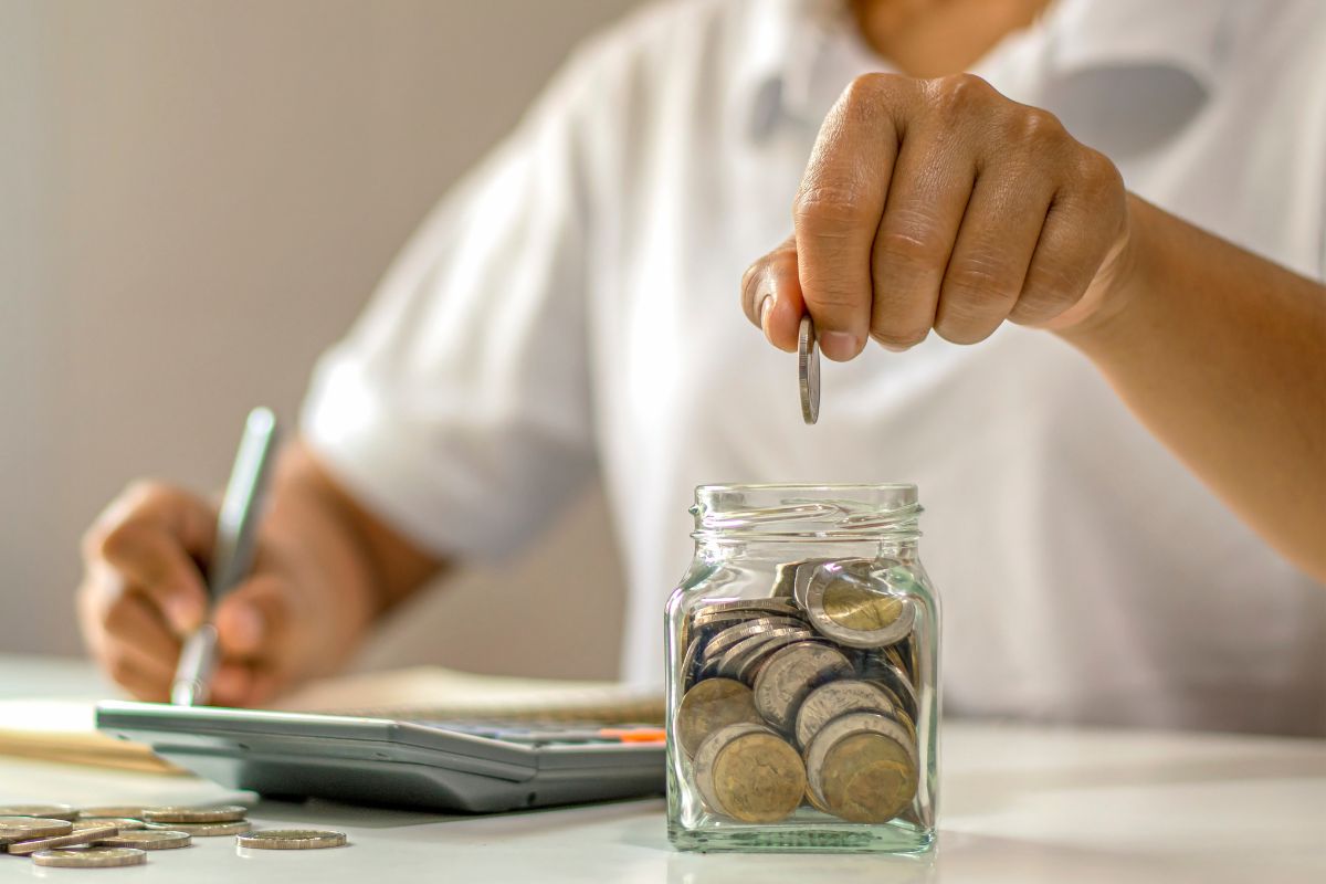A picture of someone putting coins inside a jar. 