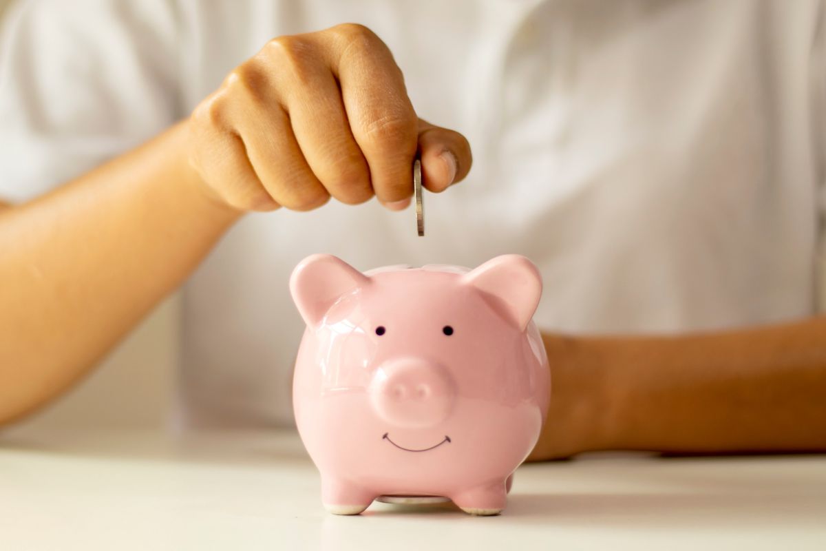 A picture of someone putting coins inside a piggy bank. 