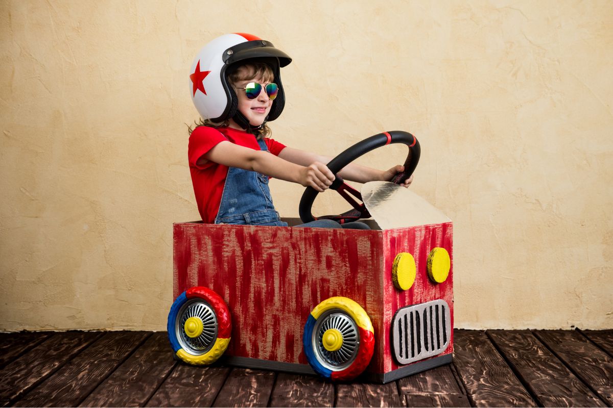 A picture of kid in a car made out of cardboard.