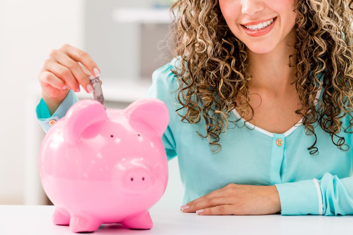 A picture of someone putting a bill in a piggy bank. 