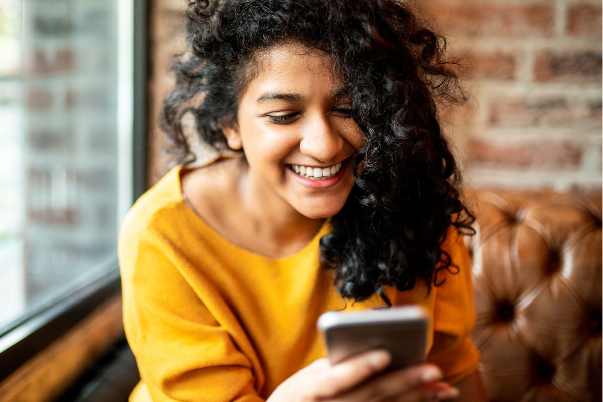 A picture of someone using their phone while smiling. 