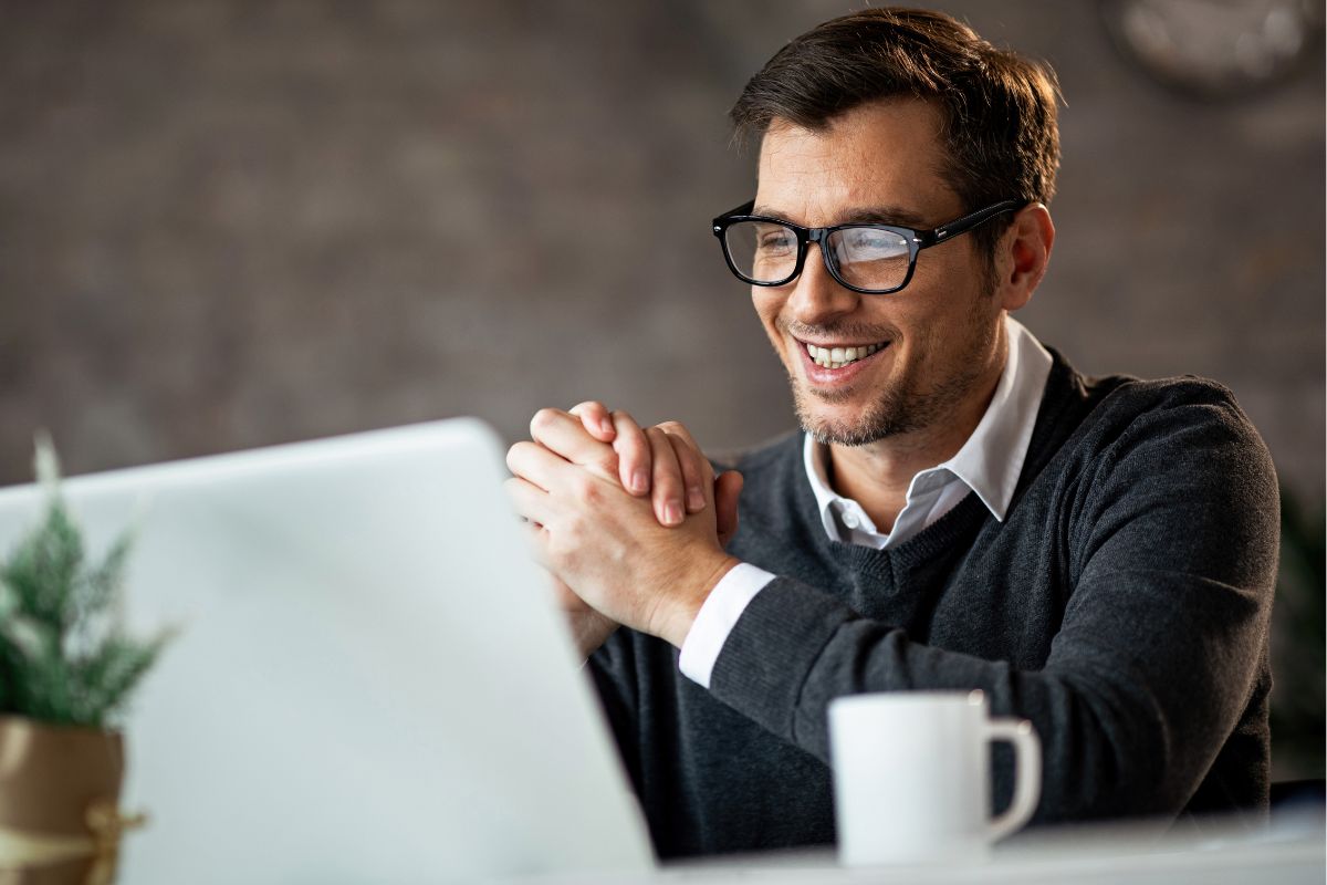 A picture of someone smiling while looking at their laptop.