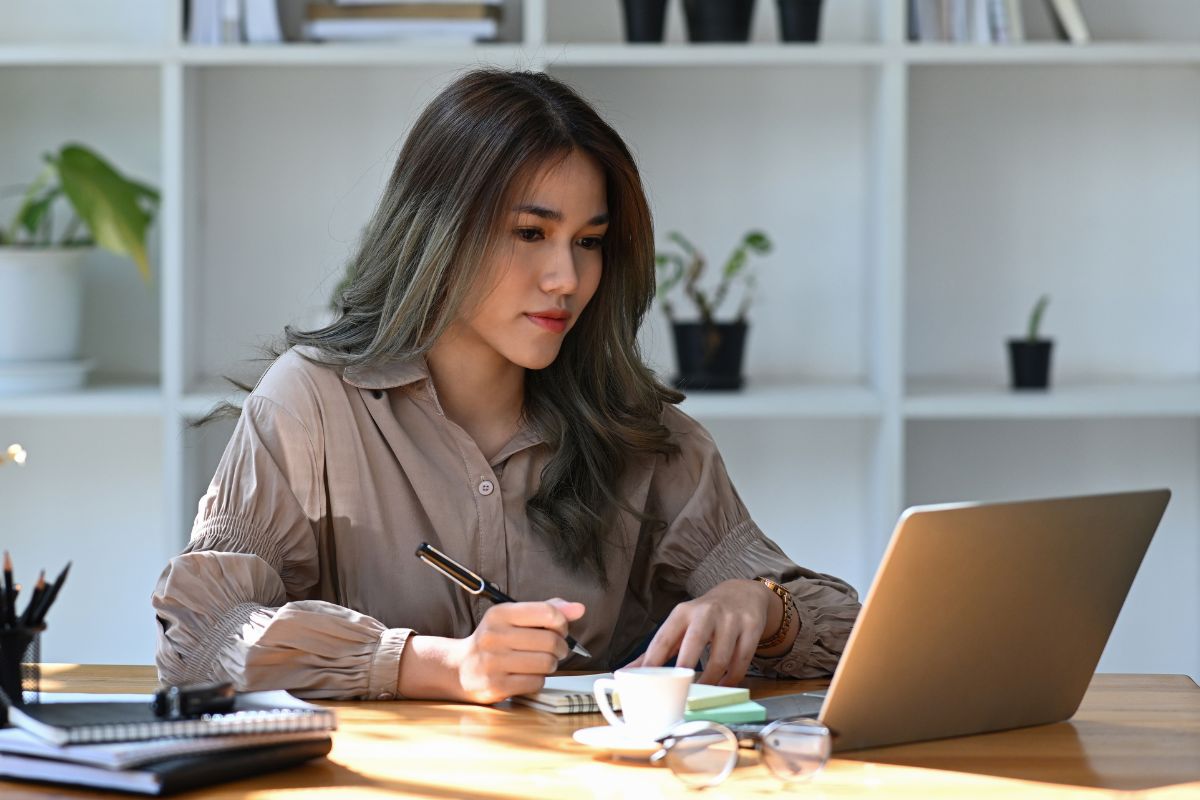 A picture of someone writing while looking at their laptop.