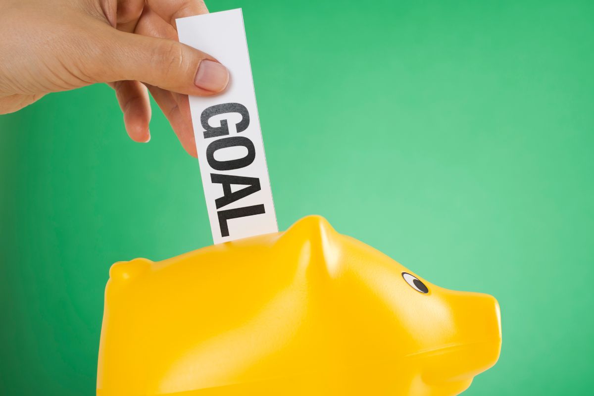 Image of a woman's hand is putting a goal paper in a piggy bank.