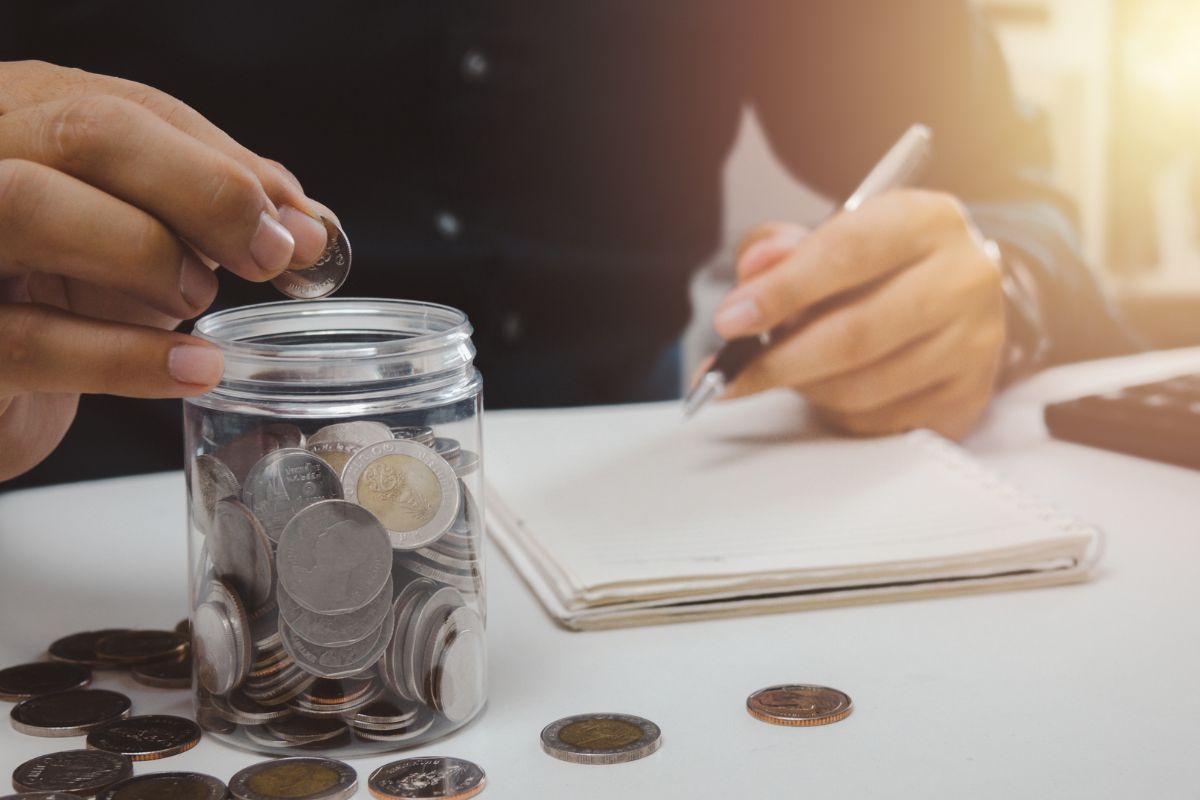 A picture of someone putting a coin in a savings jar.