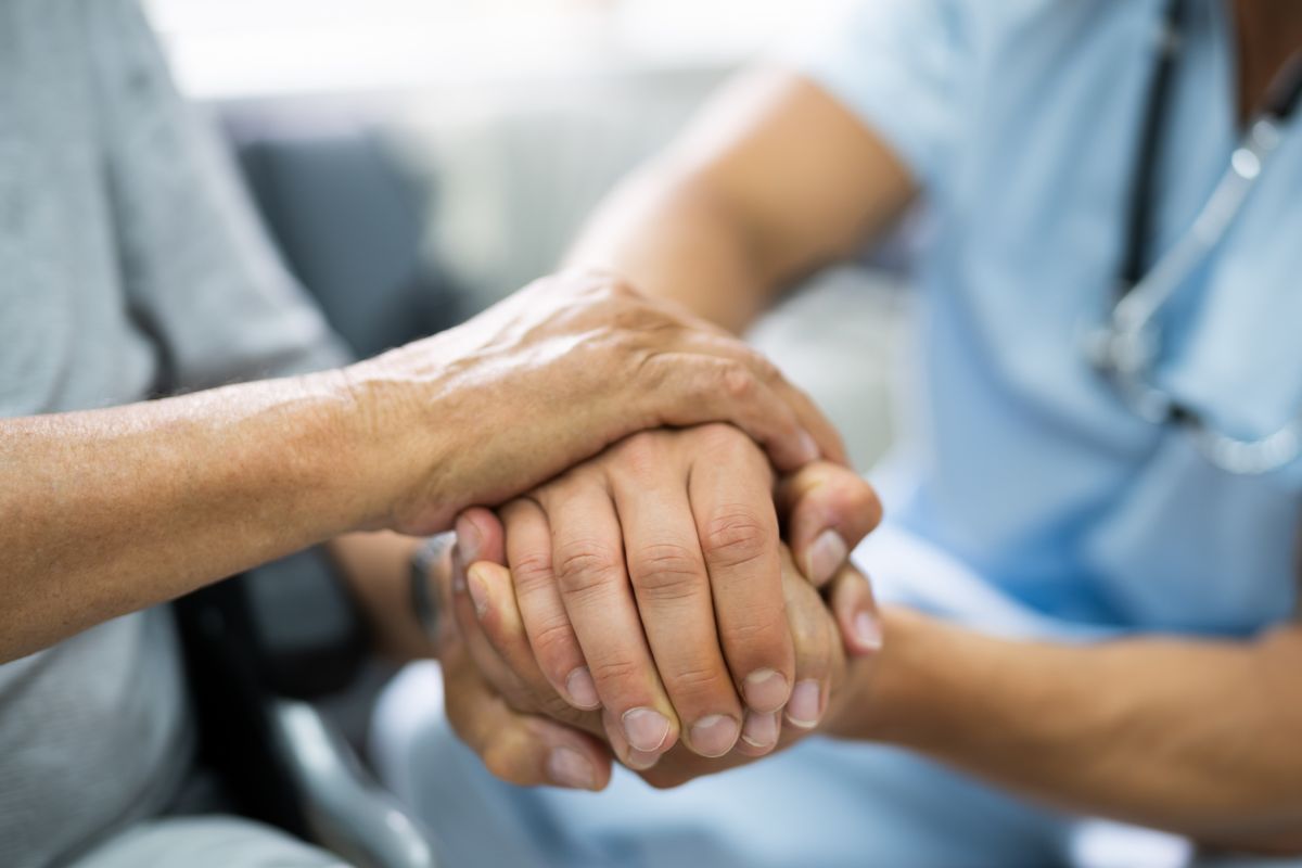 A picture of an elderly person and a healthcare worker holding hands.