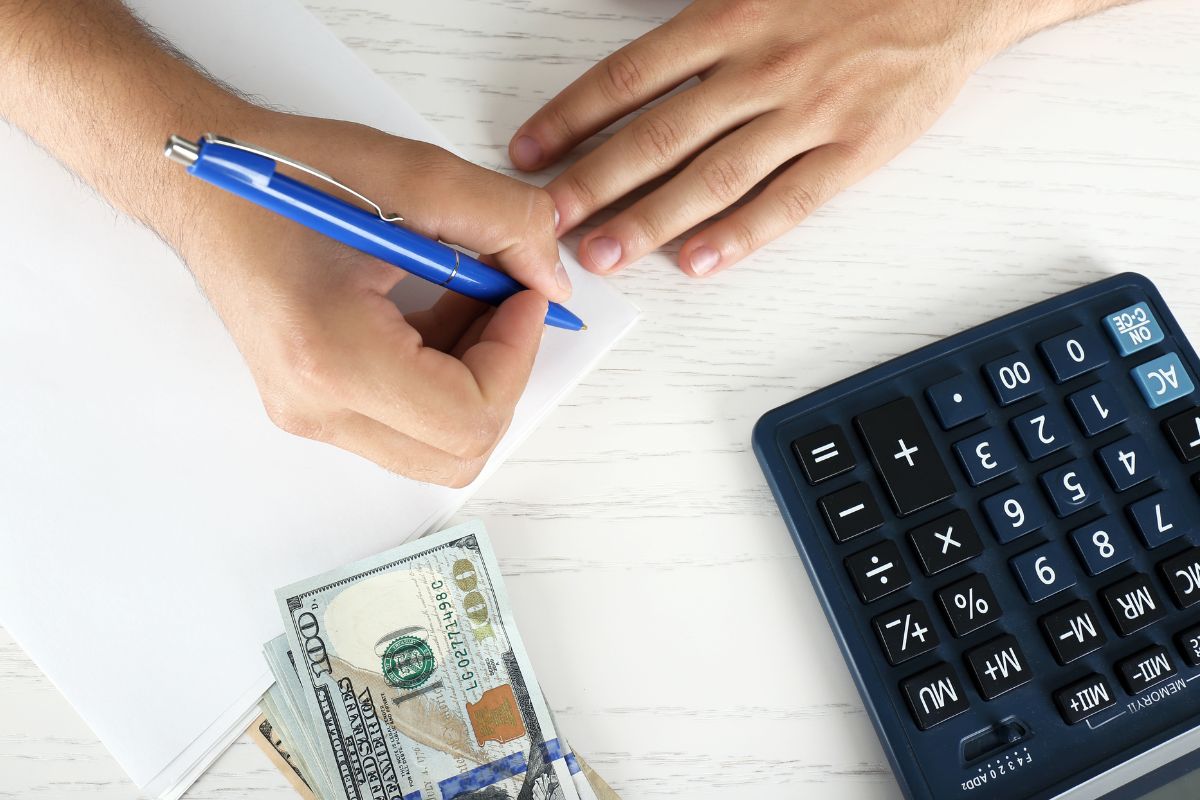An image shows a man's hand budgeting for a holiday.