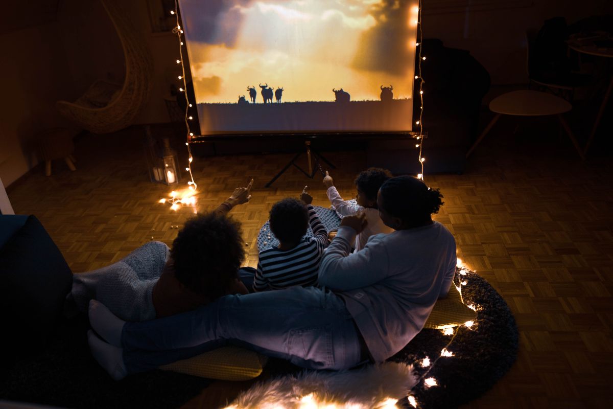 A picture of a family watching a movie on screen.