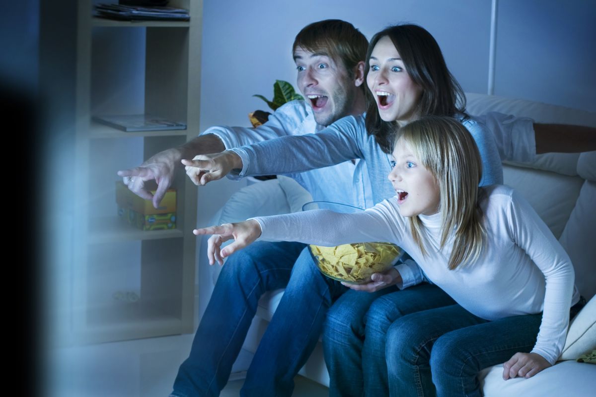 The picture shows a family watching a movie with some chips.