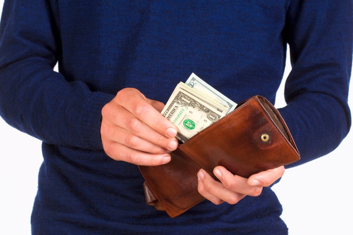 A picture of a man putting his money in his wallet.
