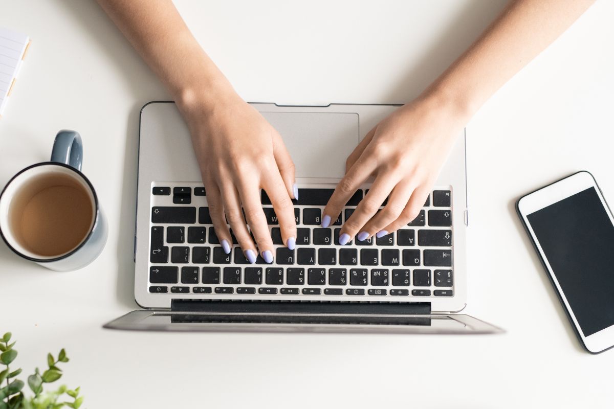 A picture of a woman's hand is typing on a laptop.