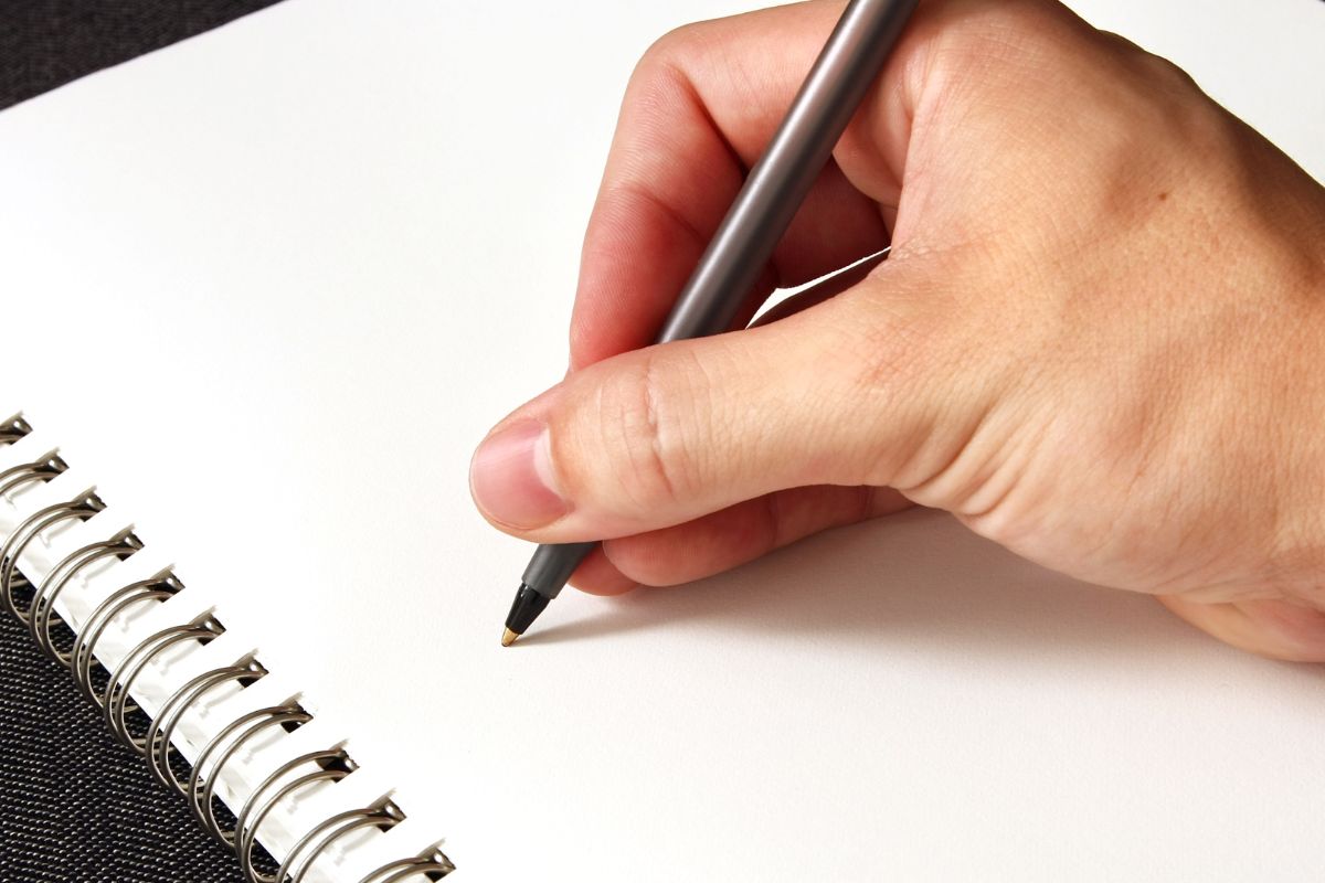 A picture of a man's hand is writing in the notebook.
