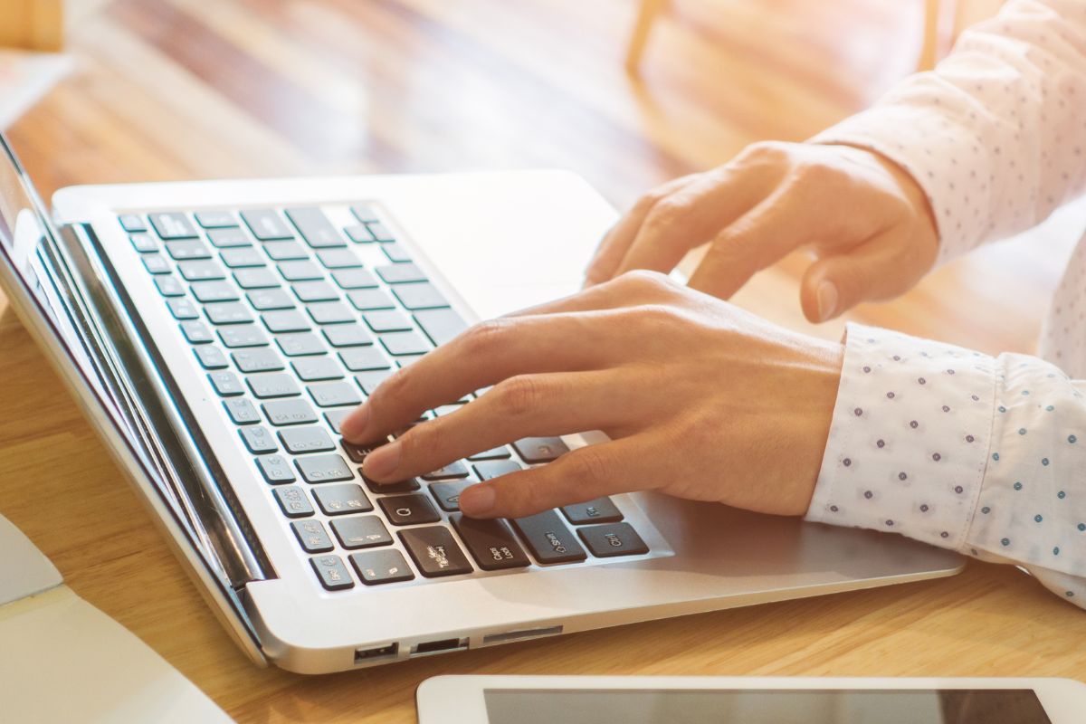 An image shows a man's hand using a laptop.