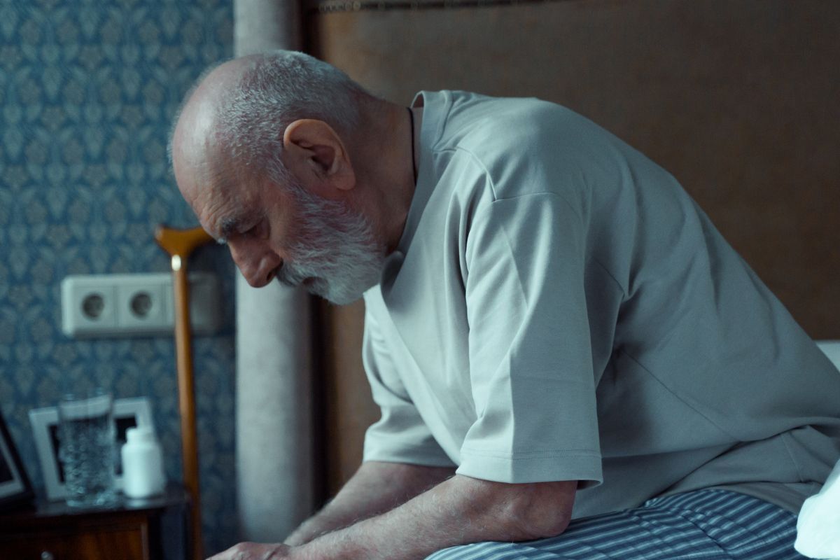 A picture of an elderly man sitting on his bed.