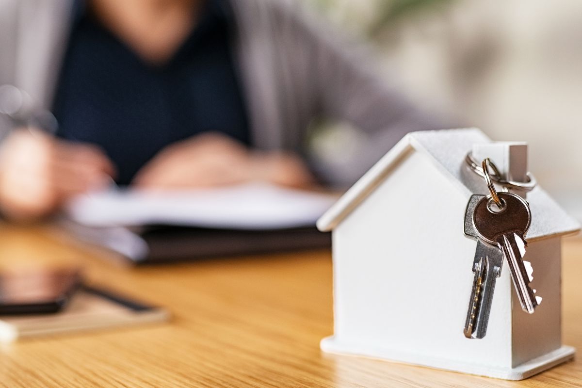 A picture shows a woman signing a paper and a mini house figure.