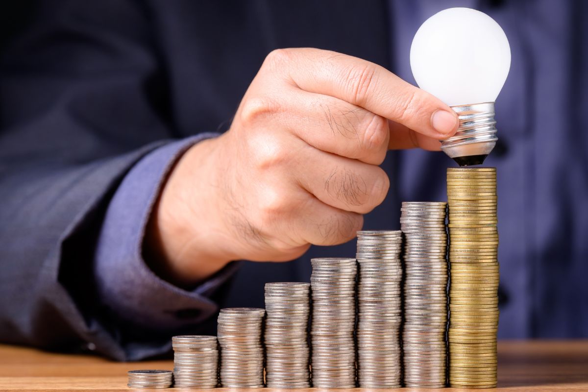 An image of a man putting a bulb on stacks of coins.
