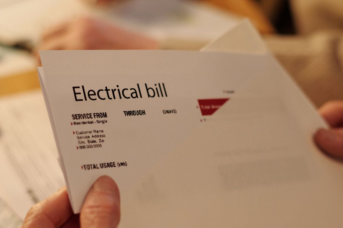 An image shows a woman's hand holding an electrical bill paper.