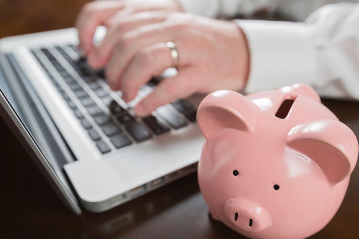 A picture shows a man typing on a laptop and a piggy bank.