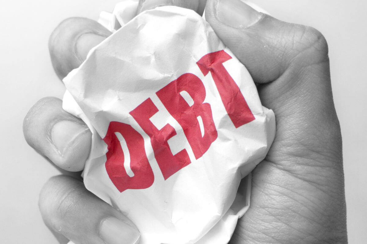 A picture shows a man's hand crumpling a paper with a debt word.