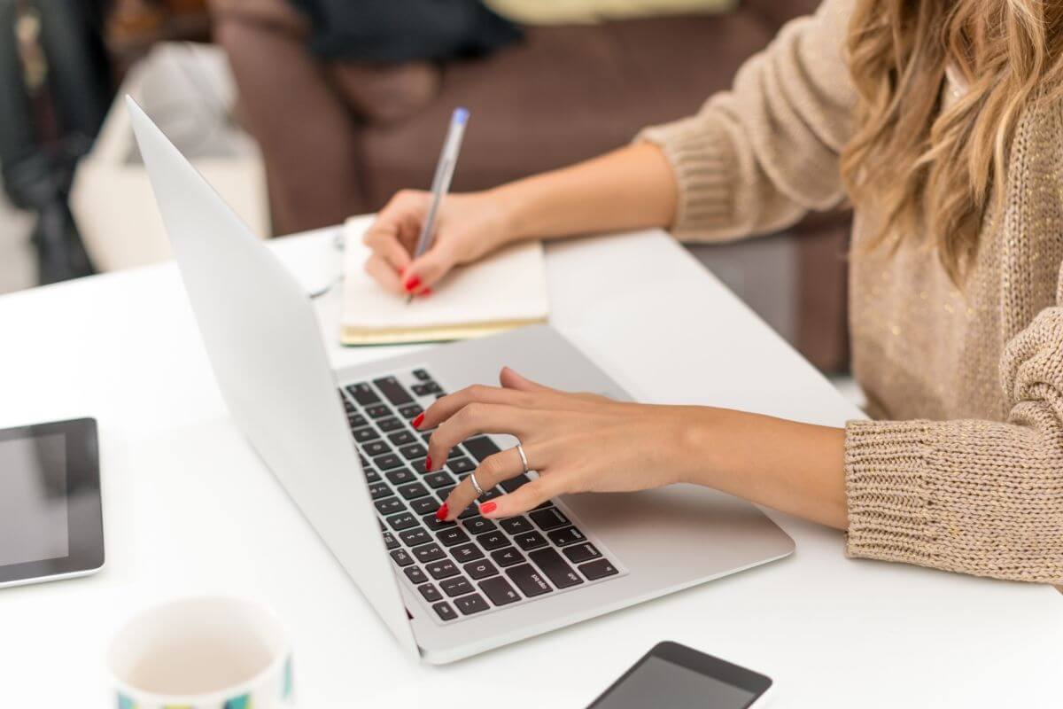 A picture of a woman using a laptop while taking notes.