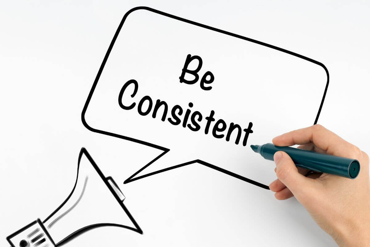 A picture shows a woman's hand writing the word 'be consistent'.