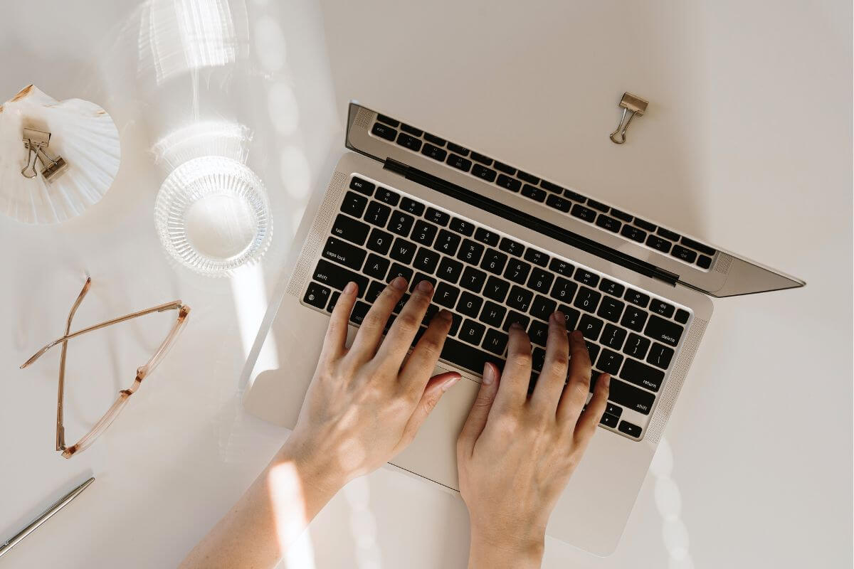 An image shows a woman's hand typing on a laptop.