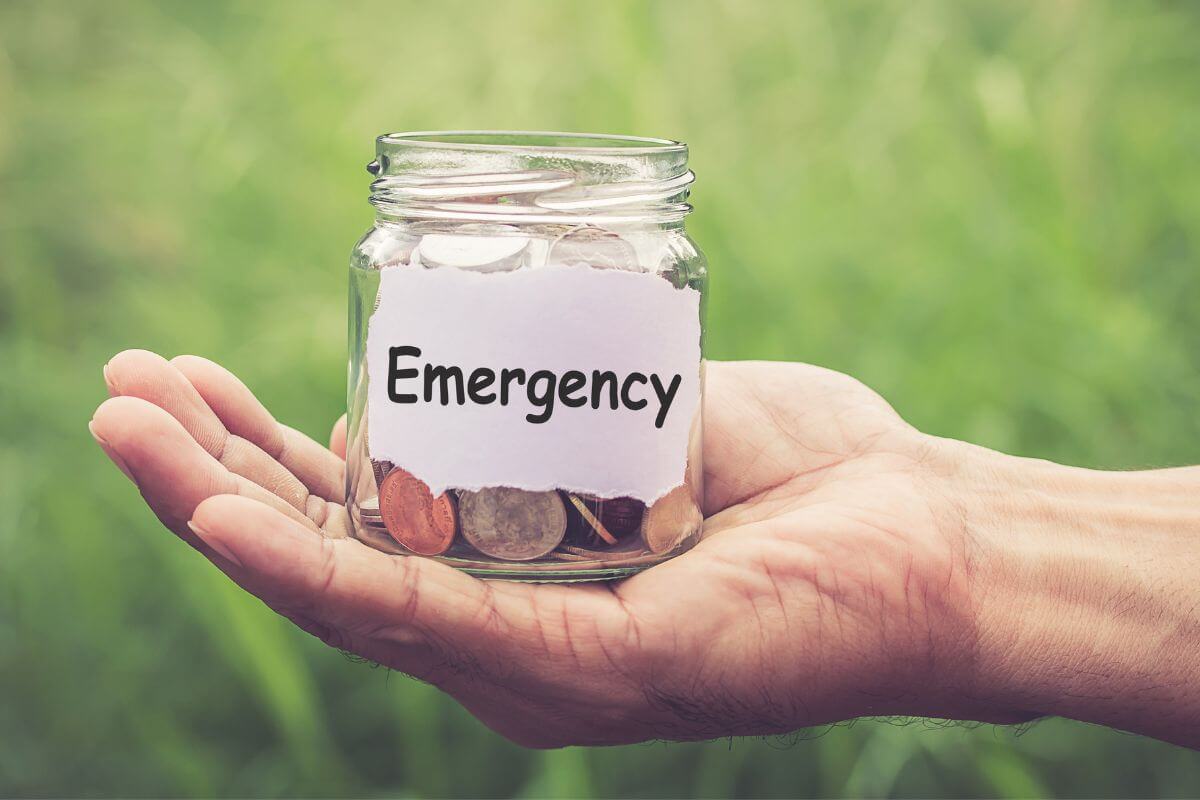 A picture shows a man's hand holding an emergency fund jar.