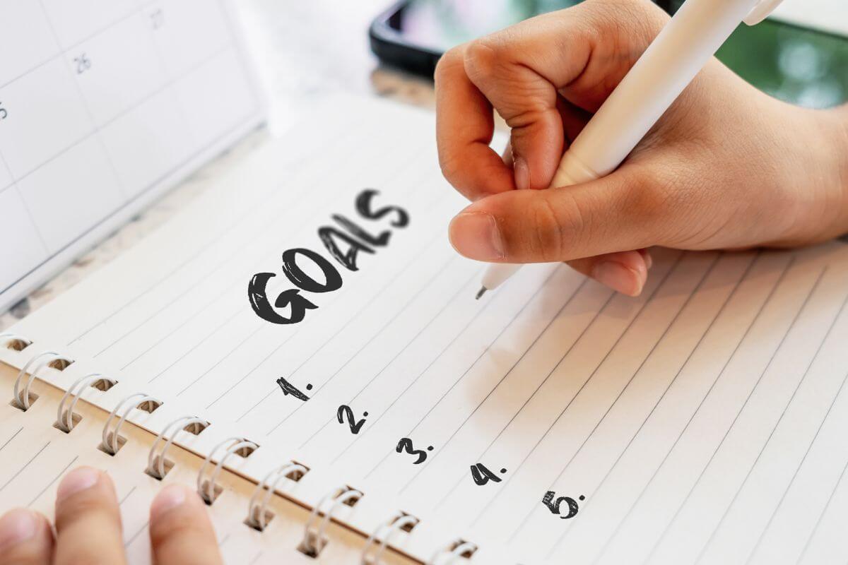 A picture shows a woman writing goals in a notebook.