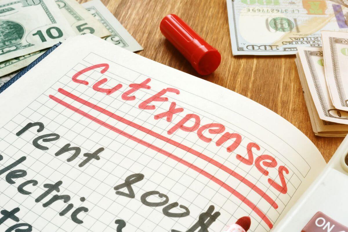 An image shows a notebook with cut expenses written on it.
