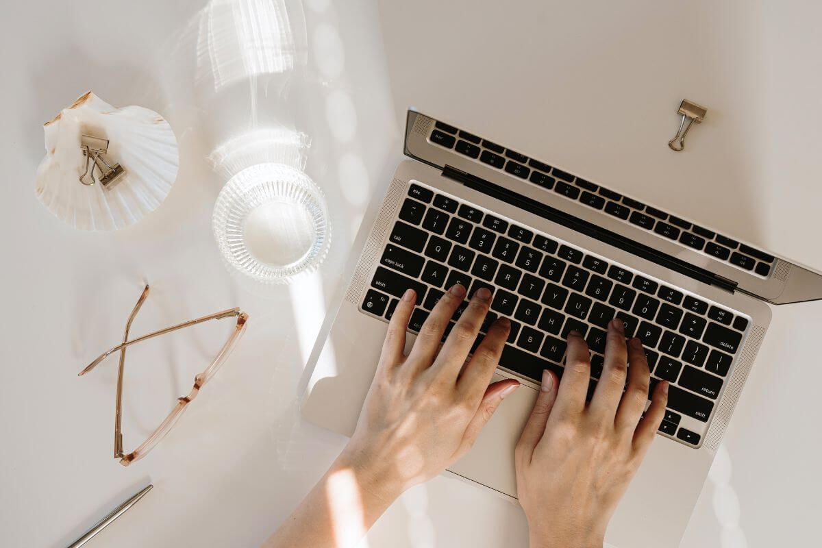 An image of a woman's hand typing on a laptop.