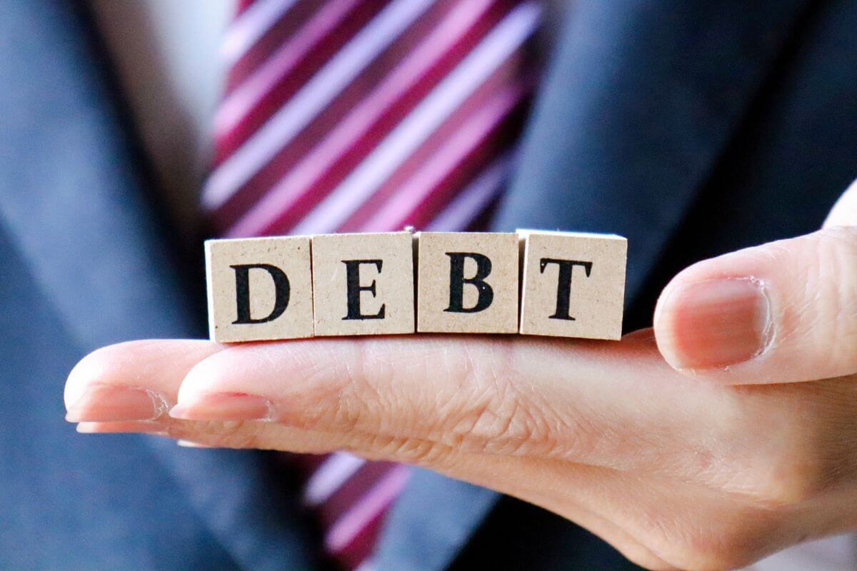 A picture of a man's hand holding wooden cubes with debt wording.
