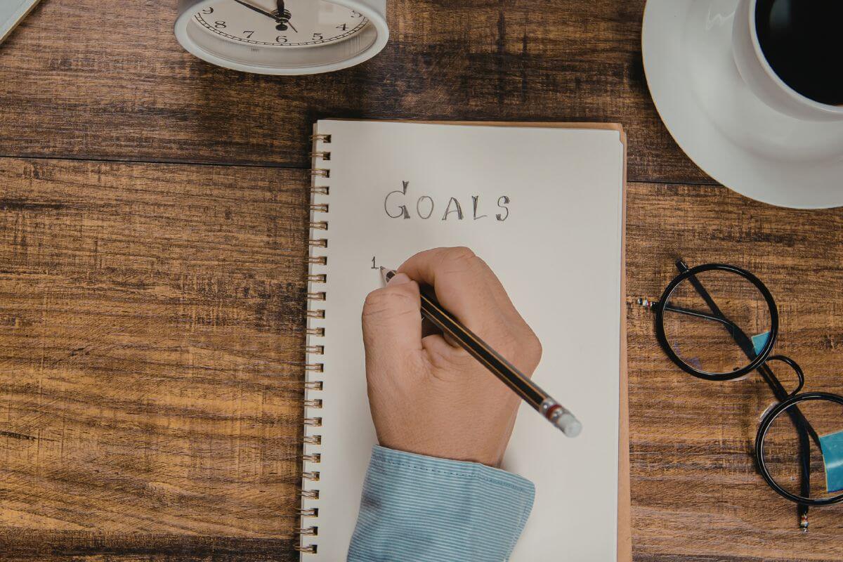 An image of a man's hand writing his goals.