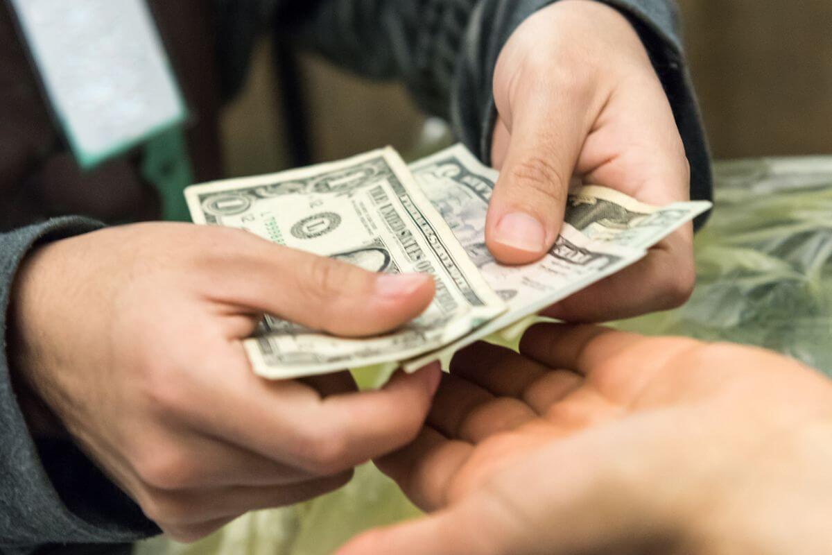 An image shows a man's hand paying with cash.