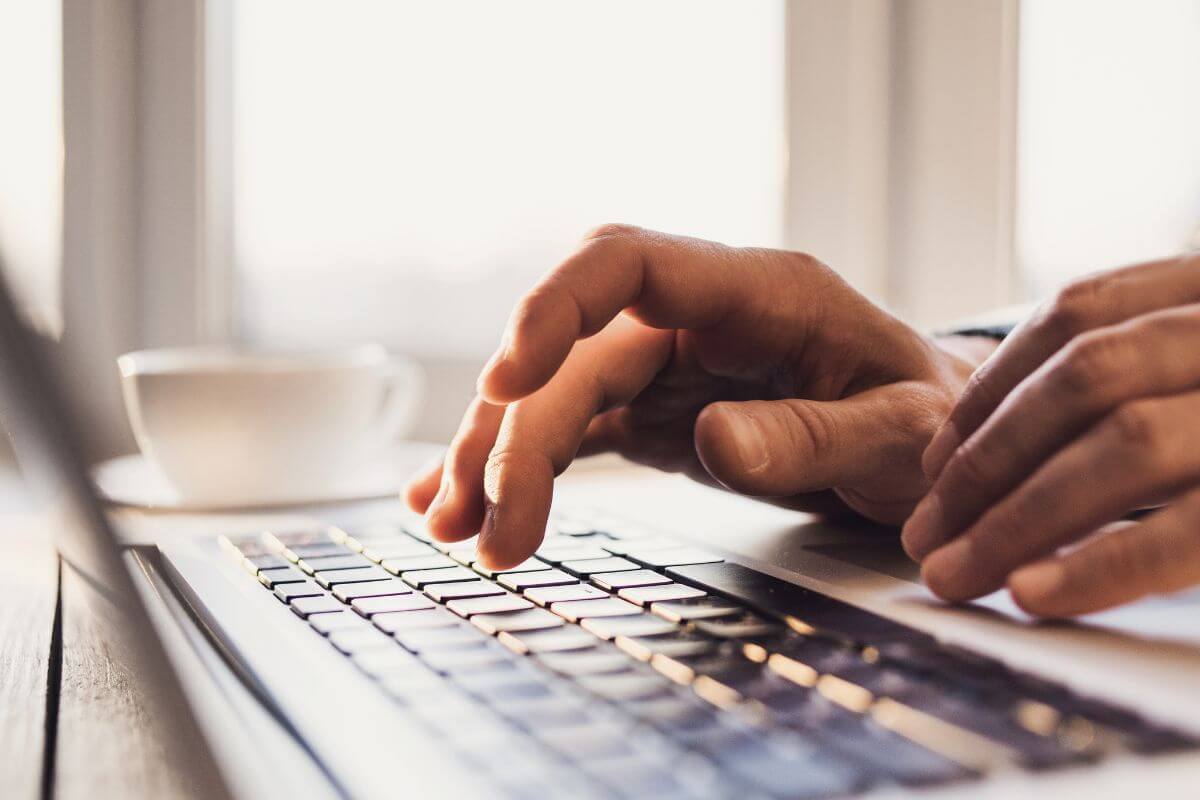 An image of a man's hand typing on a laptop.