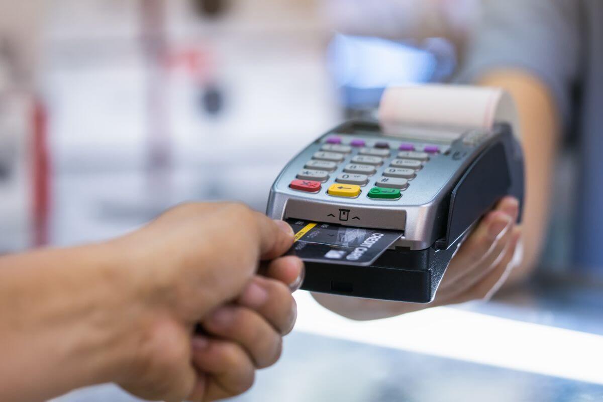 Uma imagem mostra um homem pagando com cartão de crédito. 