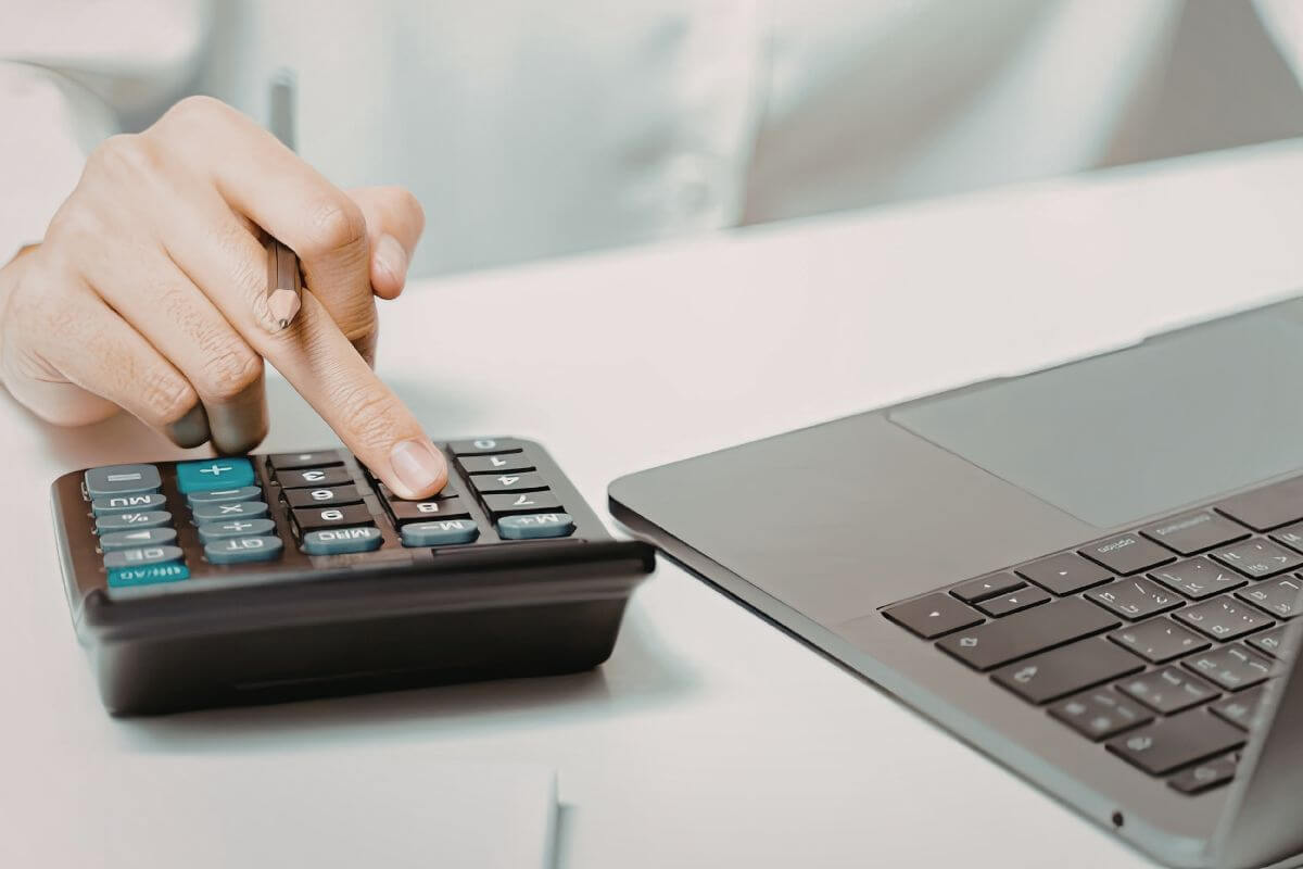 A picture of a woman's hand using a calculator and a laptop.